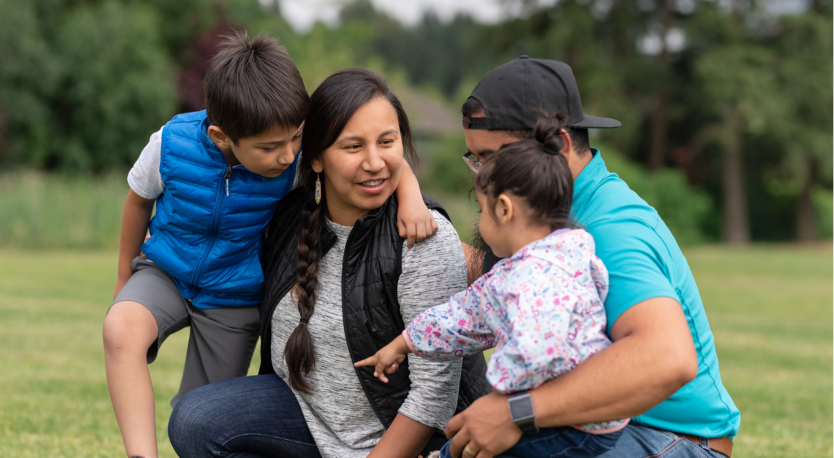 Indigenous family of four with two young children in a grassy field