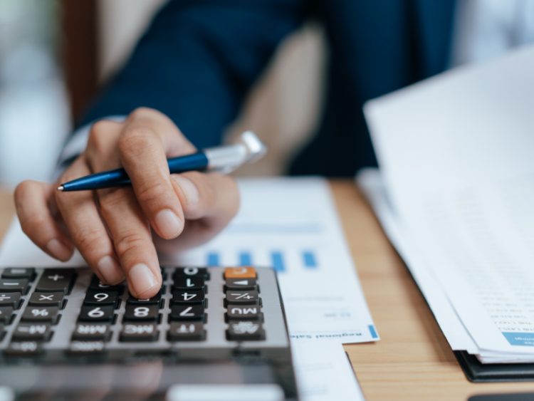 A close up of someone in a suit doing financial work with a pen and calculator