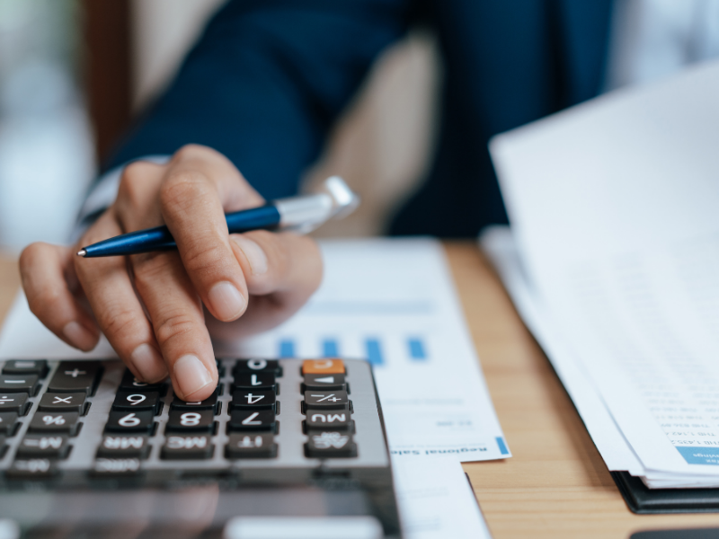 A close up of someone in a suit doing financial work with a pen and calculator